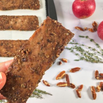 Photo of bars of the ground turkey jerky recipe on a baking sheet, surrounded by thyme, apples, and pecans (square image)
