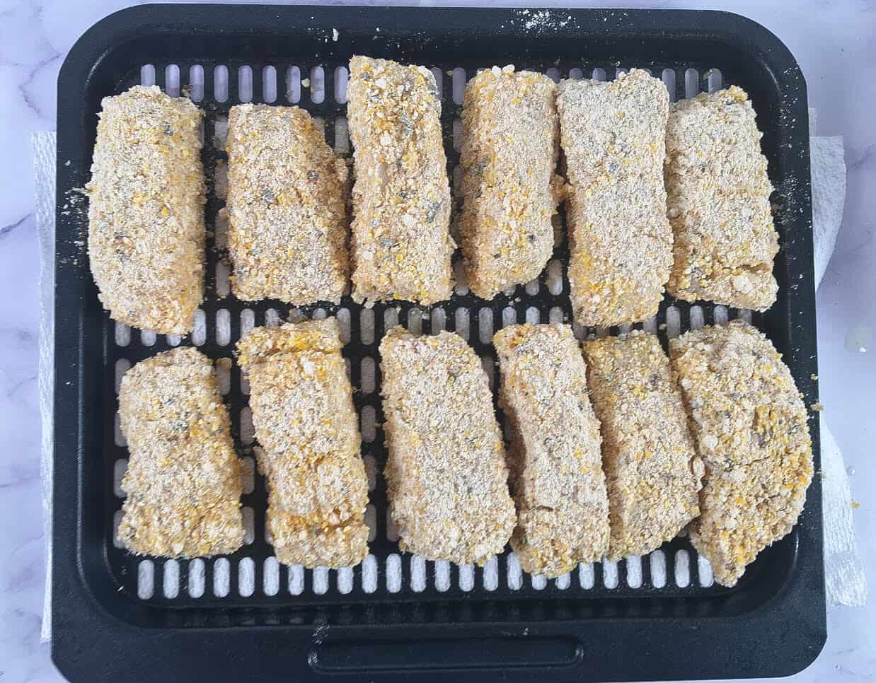 Uncooked breaded fish sticks on an air fryer tray